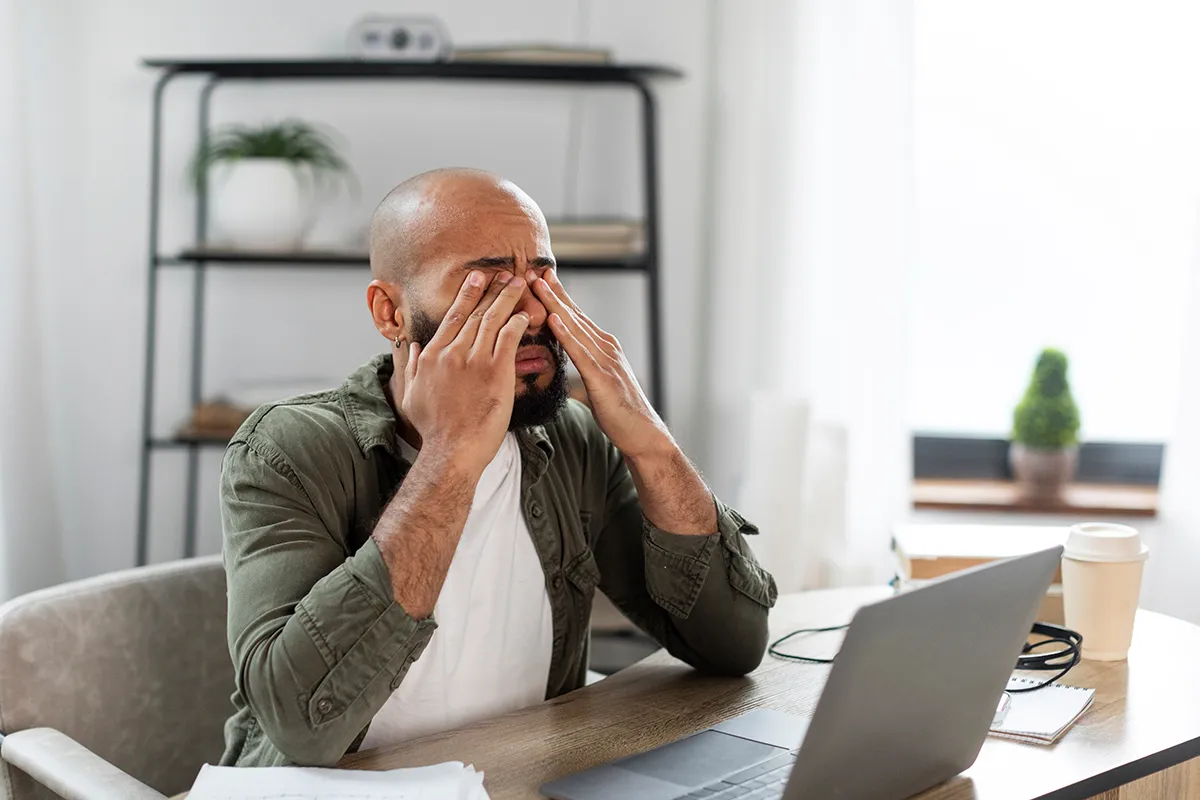 a man sitting at his desk at home and rubbing his eyes due to chronic dry eye