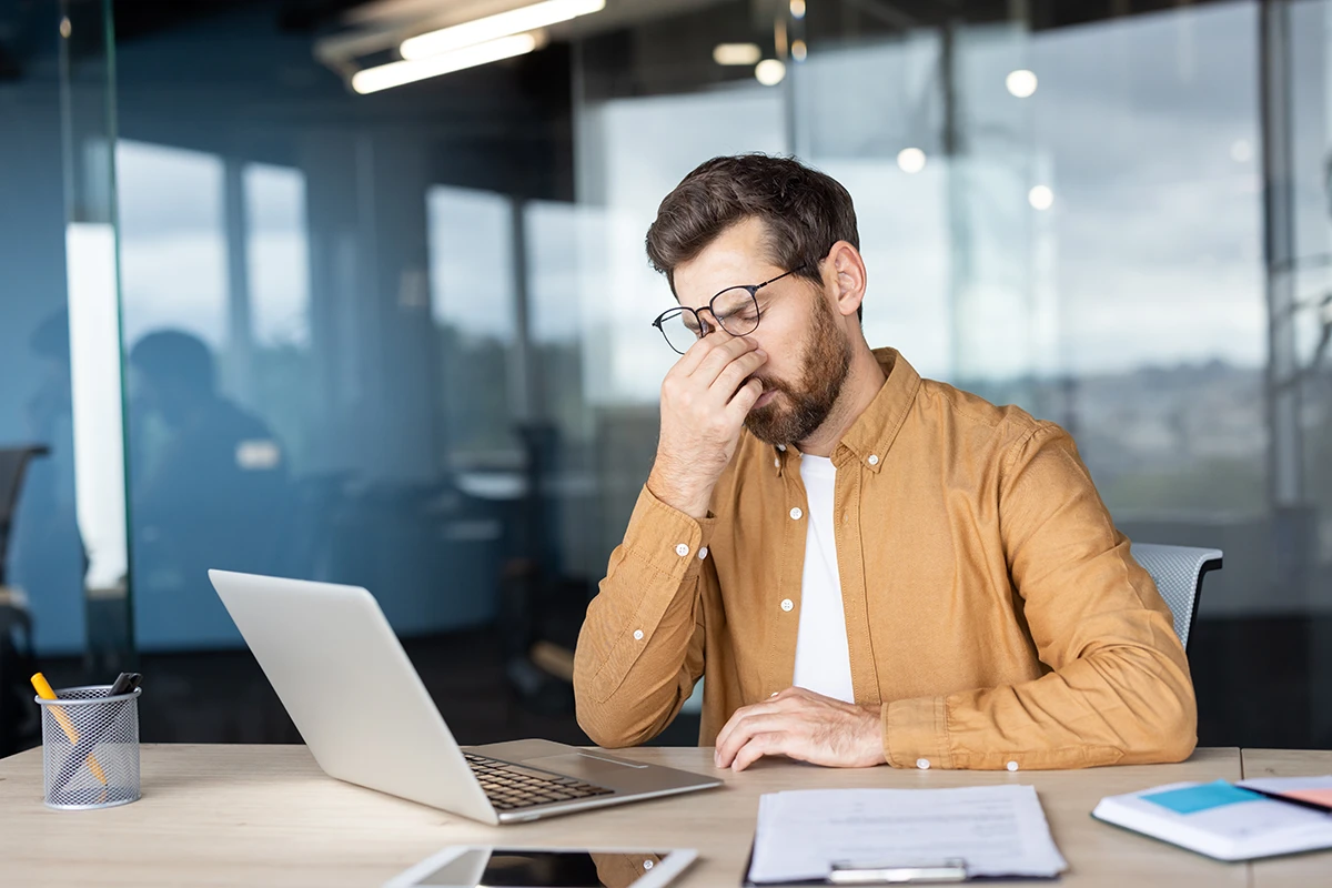 a man sitting at his desk at work and massaging the bridge of his nose due to discomfort
